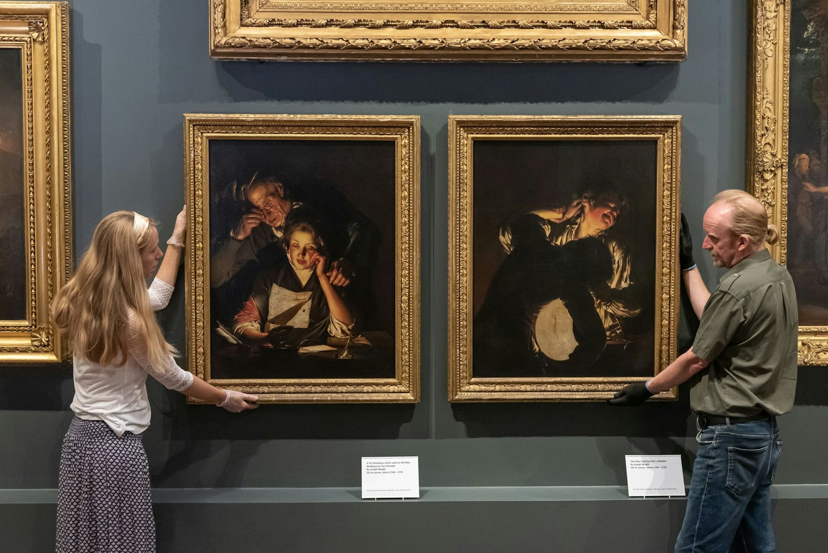 Curators Lucy Bamford (L) and Matt Edwards (R) hang ‘A Girl Reading a Letter with an Old Man Reading over her Shoulder’ and ‘Two Boys Fighting Over a Bladder’ by Joseph Wright at Derby Museum and Art Gallery