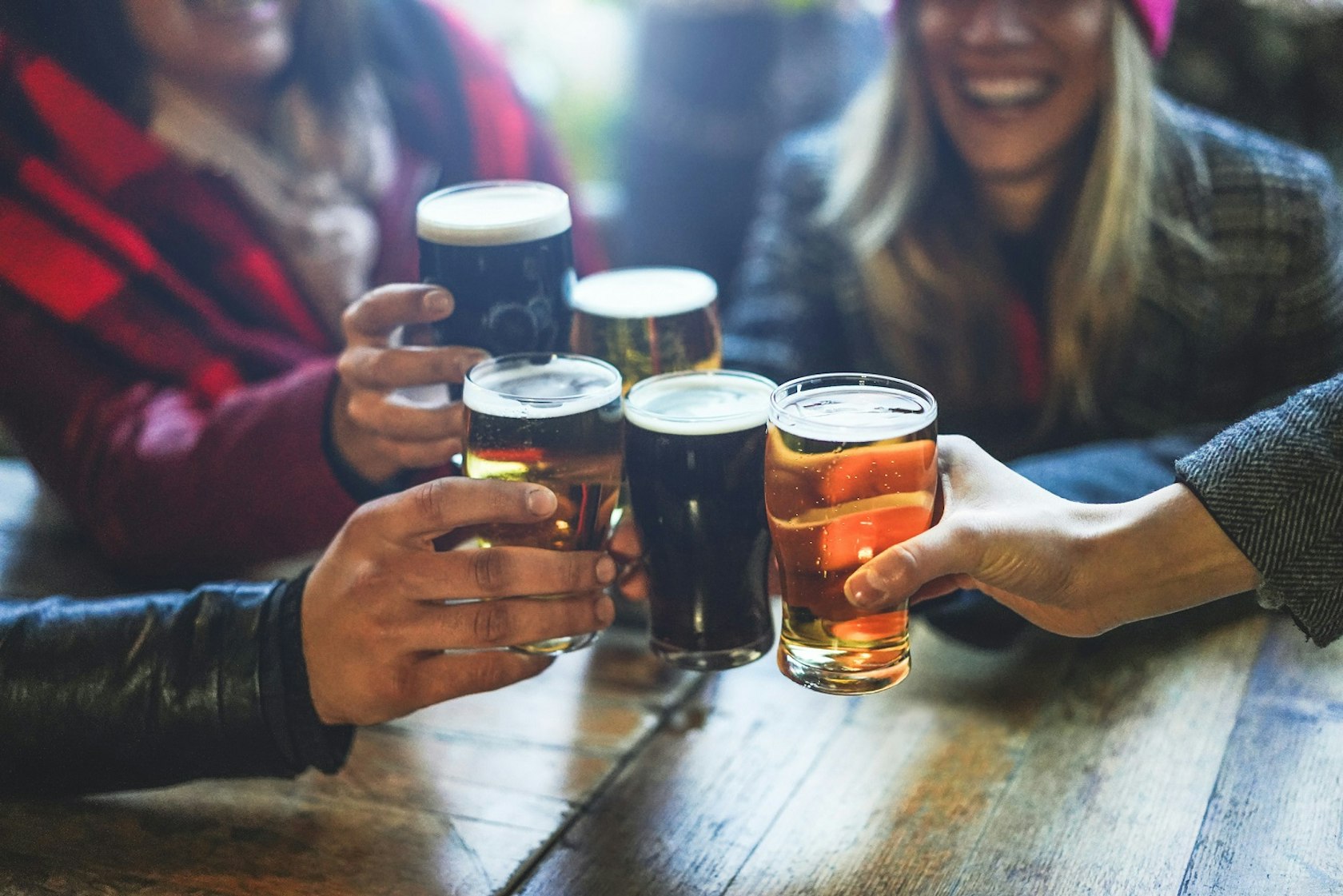 Group of happy friends drinking and toasting beer at brewery bar restaurant – Friendship concept with young people having fun together at cool vintage pub – Focus on right pint glass – High iso image