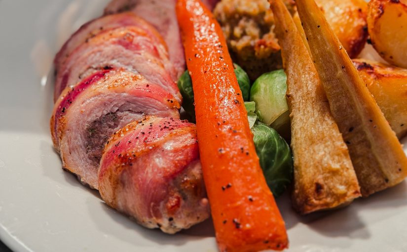 Turkey roulade with roast potatoes, maple glazed carrots & parsnips, pig in blanket, stuffing ball and turkey gravy on a white plate